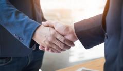 Close-up de dois profissionais em trajes sociais selando um acordo com um aperto de mão firme em um ambiente de escritório iluminado.