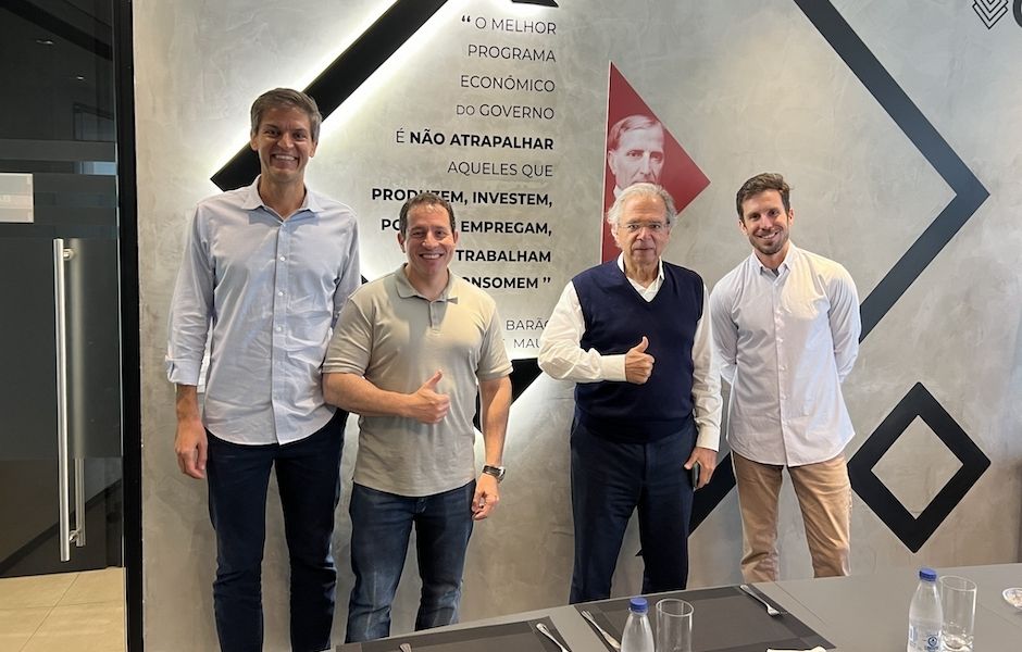 Quatro homens posam sorridentes em um escritório, incluindo o economista Paulo Guedes, diante de uma parede com uma citação sobre liberdade econômica atribuída ao Barão de Mauá.